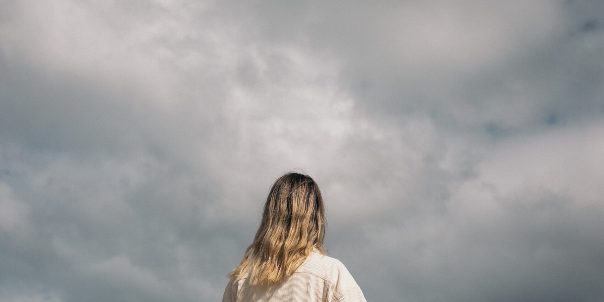 A woman standing in front of a cloudy sky. Search how online therapy can offer support with addressing seasonal affective disorder. Contact an online therapist in California for more support.