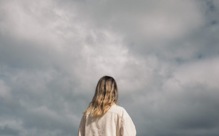A woman standing in front of a cloudy sky. Search how online therapy can offer support with addressing seasonal affective disorder. Contact an online therapist in California for more support.