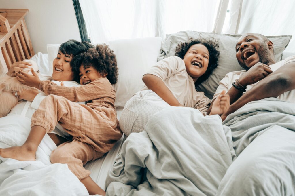 A family smiles while laughing and laying together in bed. Learn how an Asian therapist in Los Angeles, CA can offer support with neurodiversity. Search for a neurodiversity-affirming therapist in Los Angeles, CA to learn how they can offer online therapy in Los Angeles, CA or New York.