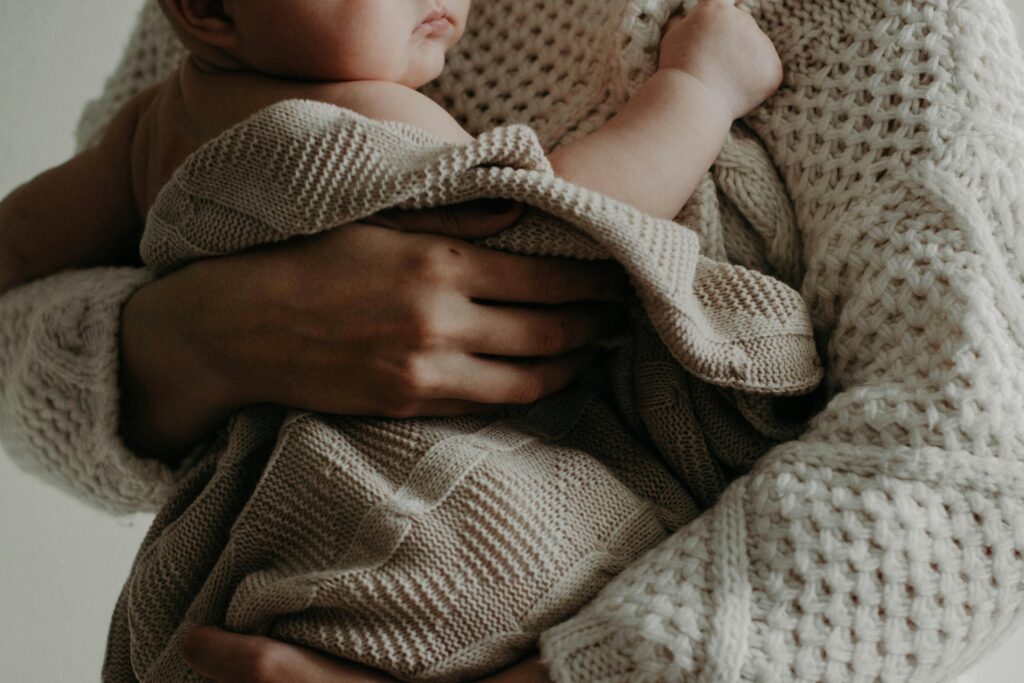 A close up of a mother holding their newborn in a blanket against their chest. This could represent the struggles of highly sensitive mothers. Learn how highly sensitive person treatment in Los Angeles, CA can offer support by searching for therapy for highly sensitive people in Los Angeles, CA today. They can offer help with postpartum therapy in los angeles and more.