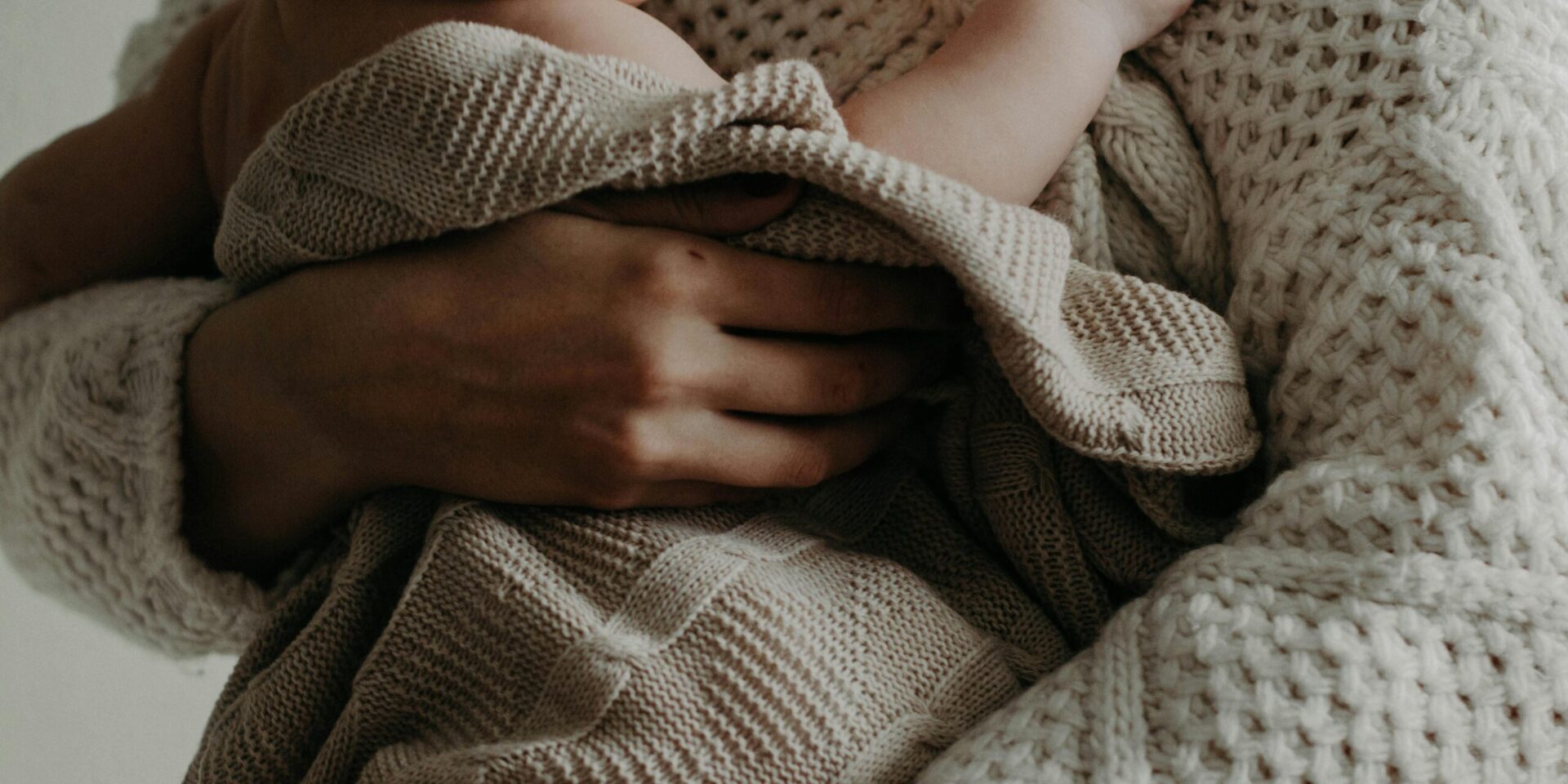 A close up of a mother holding their newborn in a blanket against their chest. This could represent the struggles of highly sensitive mothers. Learn how highly sensitive person treatment in Los Angeles, CA can offer support by searching for therapy for highly sensitive people in Los Angeles, CA today. They can offer help with postpartum therapy in los angeles and more.