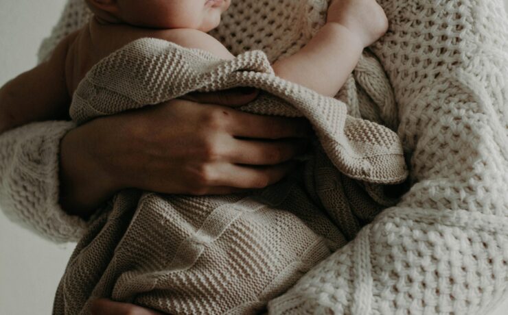 A close-up photo of a woman holding a baby, without their faces visible. Learn how a sensitivity-affirming therapist can help highly sensitive mom's today. Search online for sensitivity-affirming therapistst in Los Angeles and New York for more information.