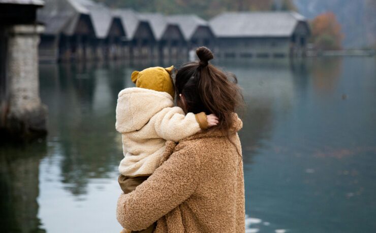 A woman holding a toddler, looking out onto a lake, with their backs to the viewer. Learn how a sensitivity-affirming therapist can help highly sensitive mom's today. Search online for sensitivity-affirming therapistst in Los Angeles and New York for more information.