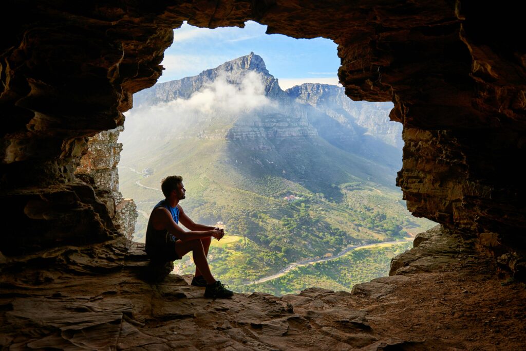 A man sits at the entrance of a cave, gazing out at a breathtaking mountain landscape with misty peaks and lush greenery. Learn more about the support an Asian American therapist in Los Angeles can offer. Contact a burnout therapist in Los Angeles, CA to start burnout treatment and other services.
