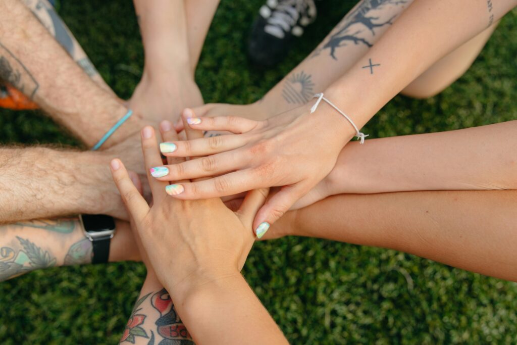 An image of many hands with different skin tones and apperances, overlapping one another over a grassy area. An image that illustrates the way our many different identities intersect.