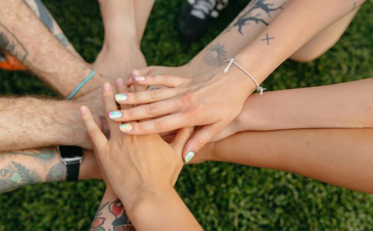 An image of many hands with different skin tones and apperances, overlapping one another over a grassy area. An image that illustrates the way our many different identities intersect.