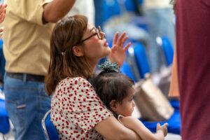pexels-israwmx-24023656 A young mother and her child sitting in her lap at what seems to be a religious gathering