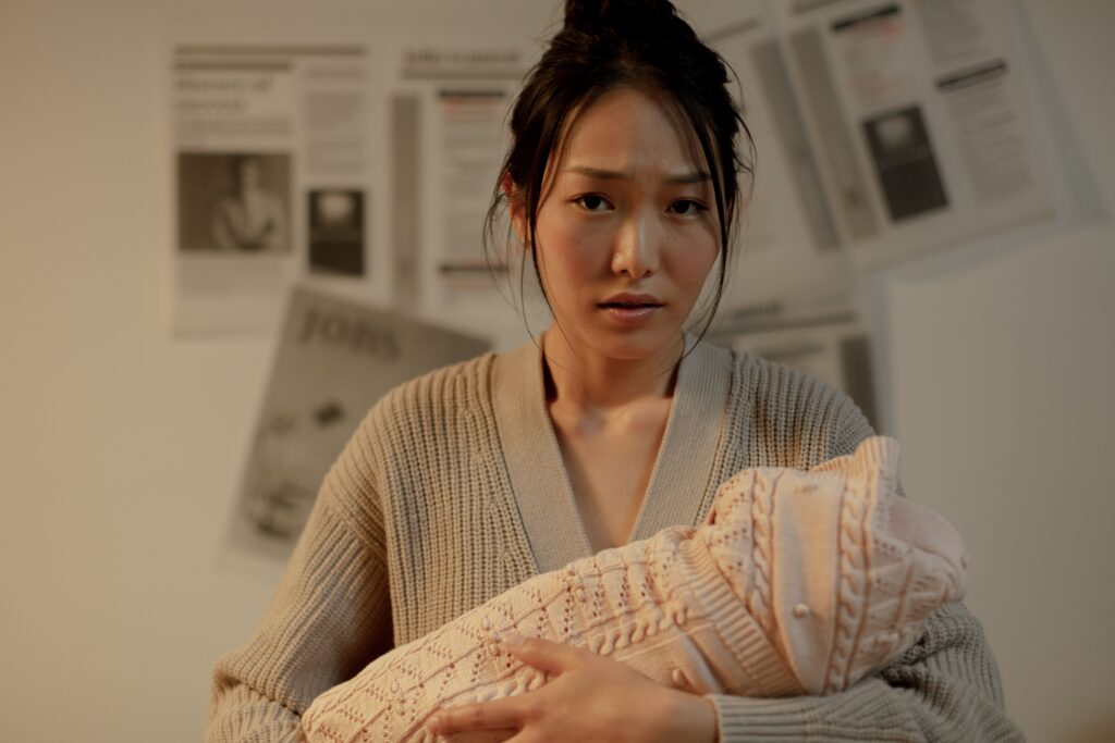 An Asian woman holding her newborn baby and looking distressed