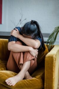 pexels-timur-weber-8560844 A young woman sitting with her head buried in her knees on the couch