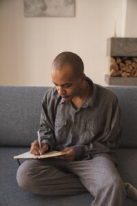 A young man sits on the couch writing in a journal.