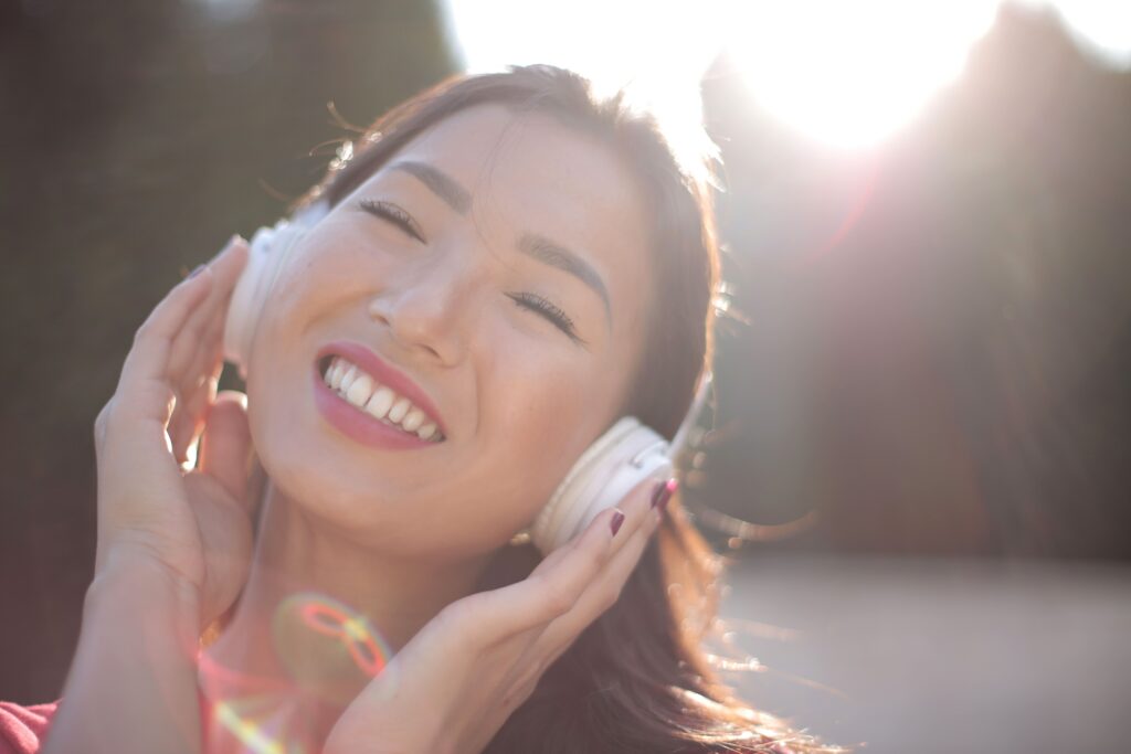 An Asian woman is smiling happily with eyes closed in the sunlight, listening to music.